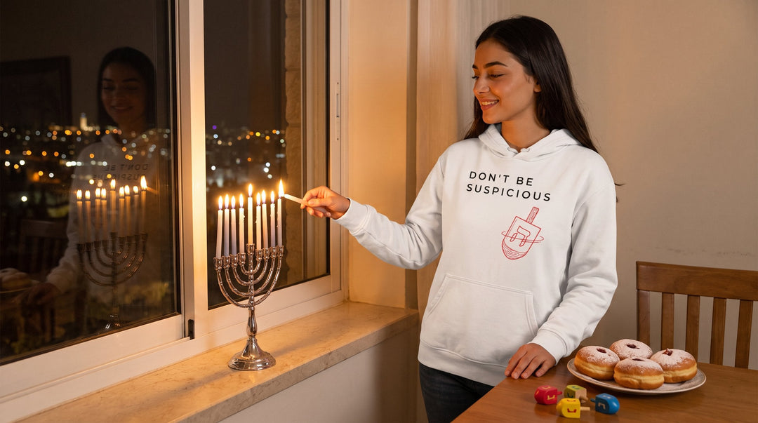 Woman in a Don't Be Suspicious Dreidel hoodie lighting a Hanukkah menorah at a window overlooking Jerusalem at night