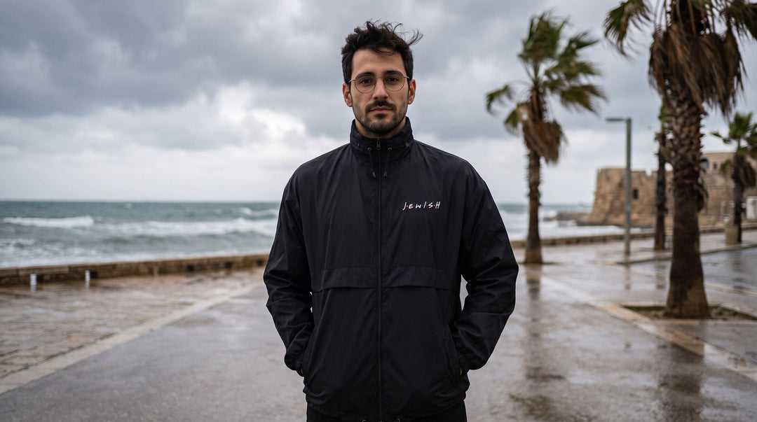 Man wearing the J.E.W.I.S.H. windbreaker on a windy beach promenade - emohtee men windbreakers