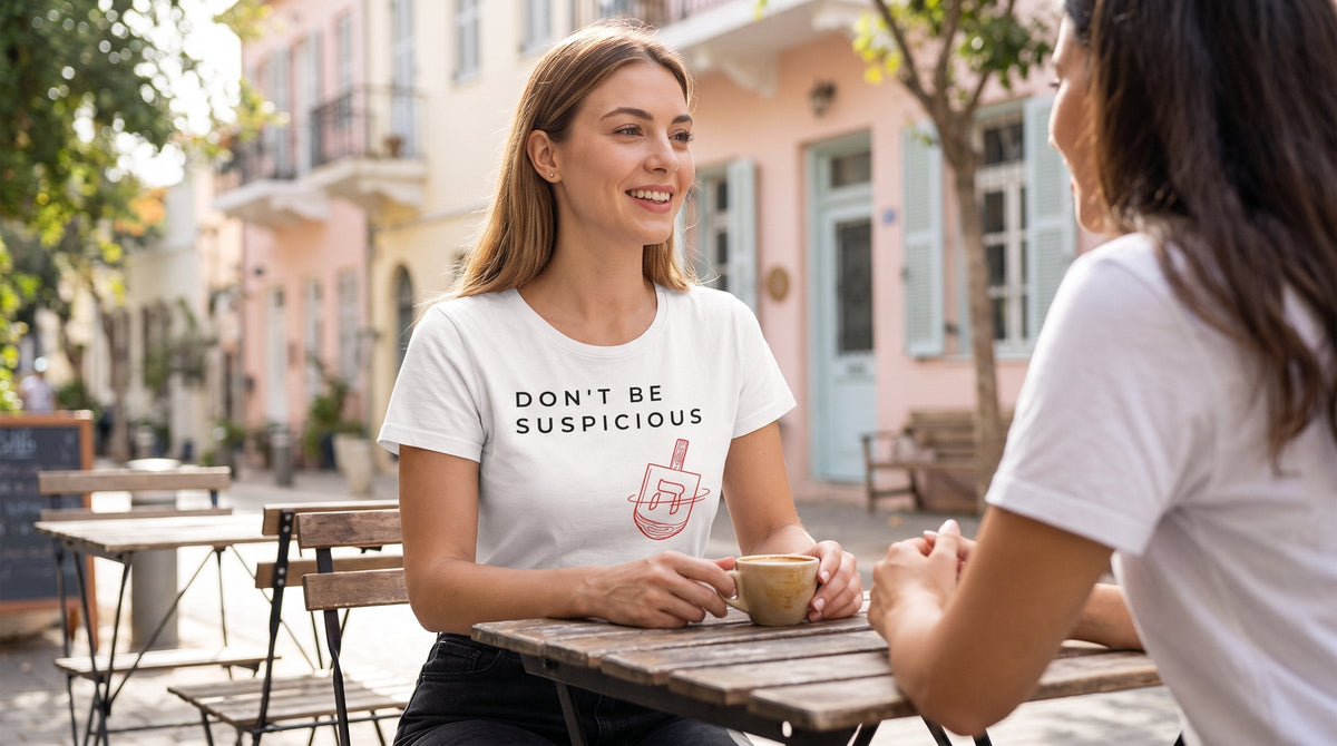 Don't Be Suspicious Dreidel T-shirt worn by a woman in the pastel lanes of Neve Tzedek, Tel Aviv – MoT Member of the Tribe
