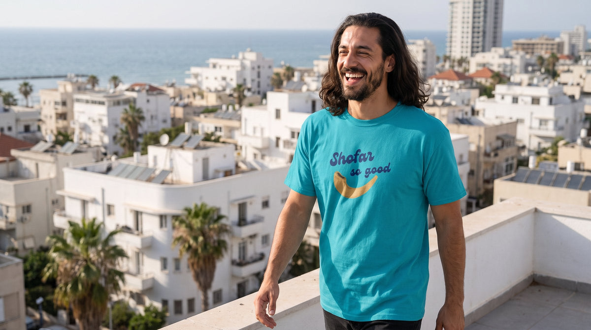 Shofar So Good T-shirt worn by a man on a rooftop terrace above the Tel Aviv skyline – MoT Member of the Tribe